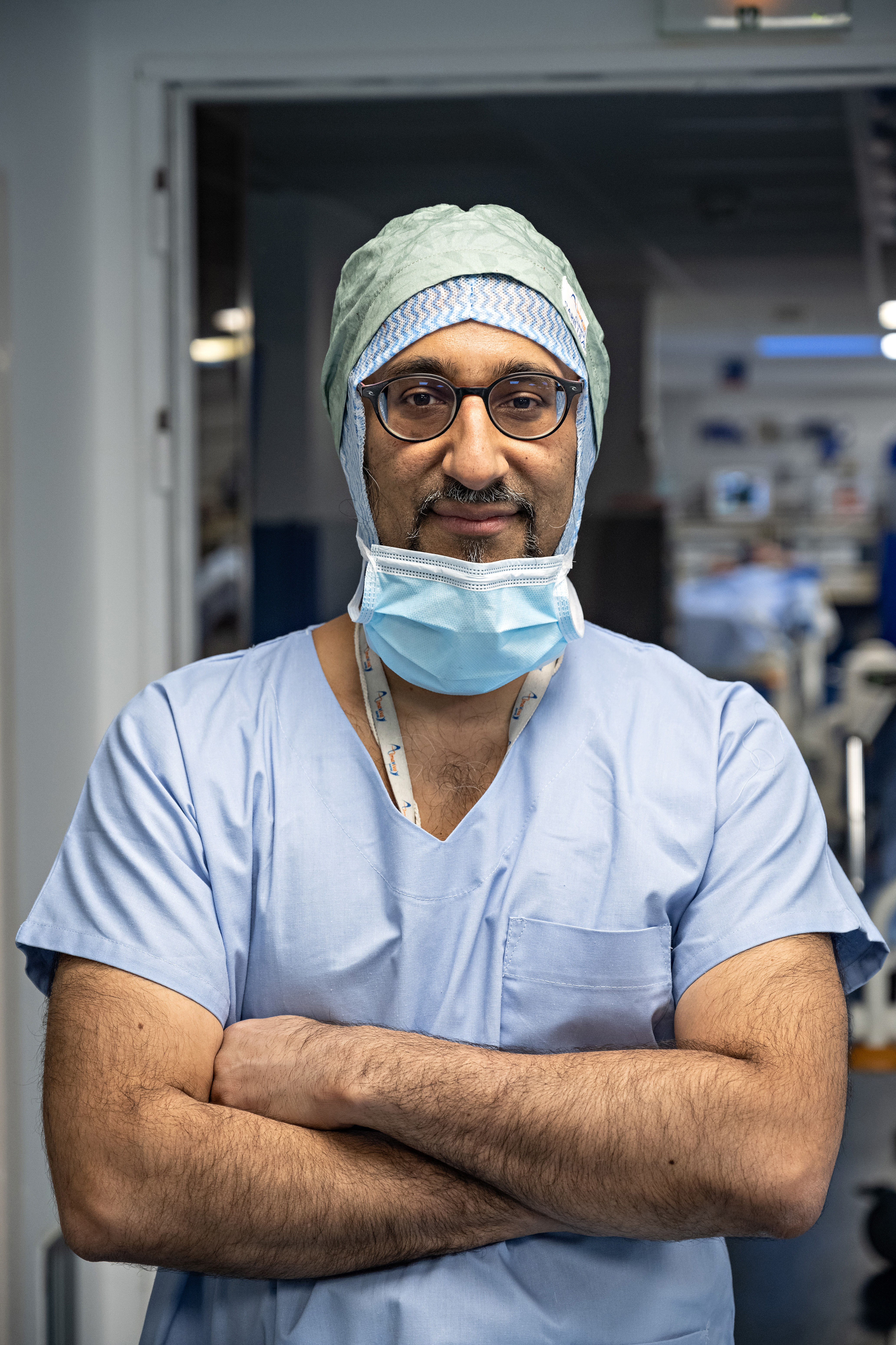 Dr Moussadjy en tenue de bloc chirurgicale bleue, bras croisés, regard direct et assuré